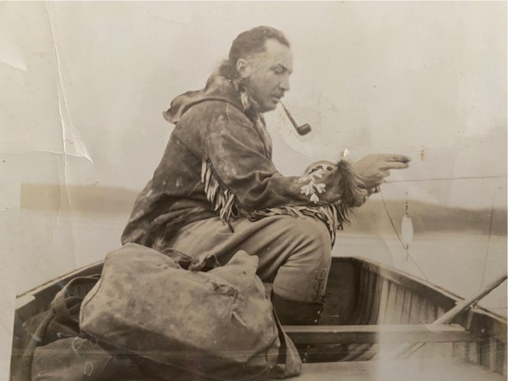 Sepia-toned photograph of Jack Leve sitting in a rowboat wearing a fringed jacket and smoking a pipe.